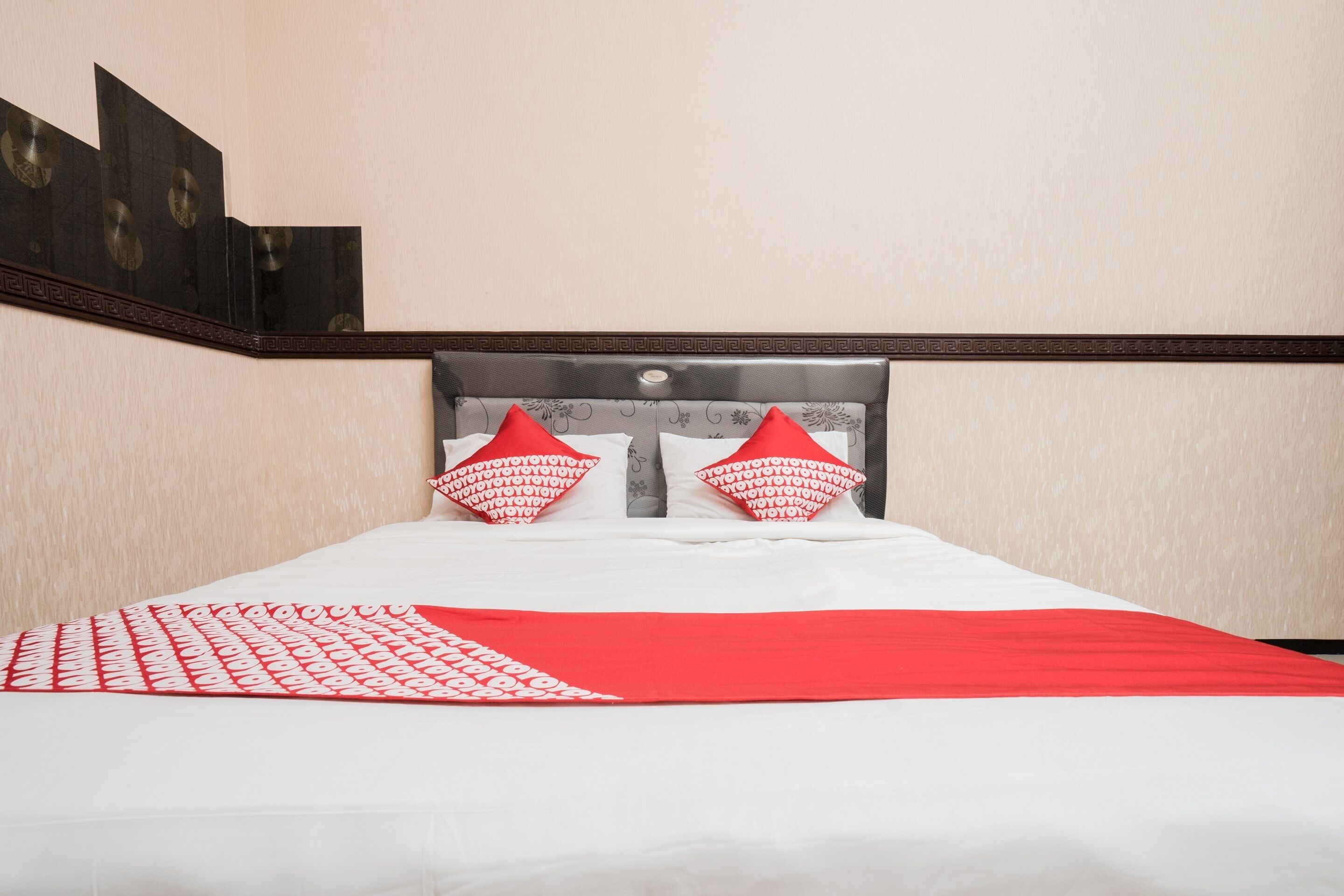 A neatly made bed with a white and red bedspread, two red pillows, and a headboard with a decorative pattern.