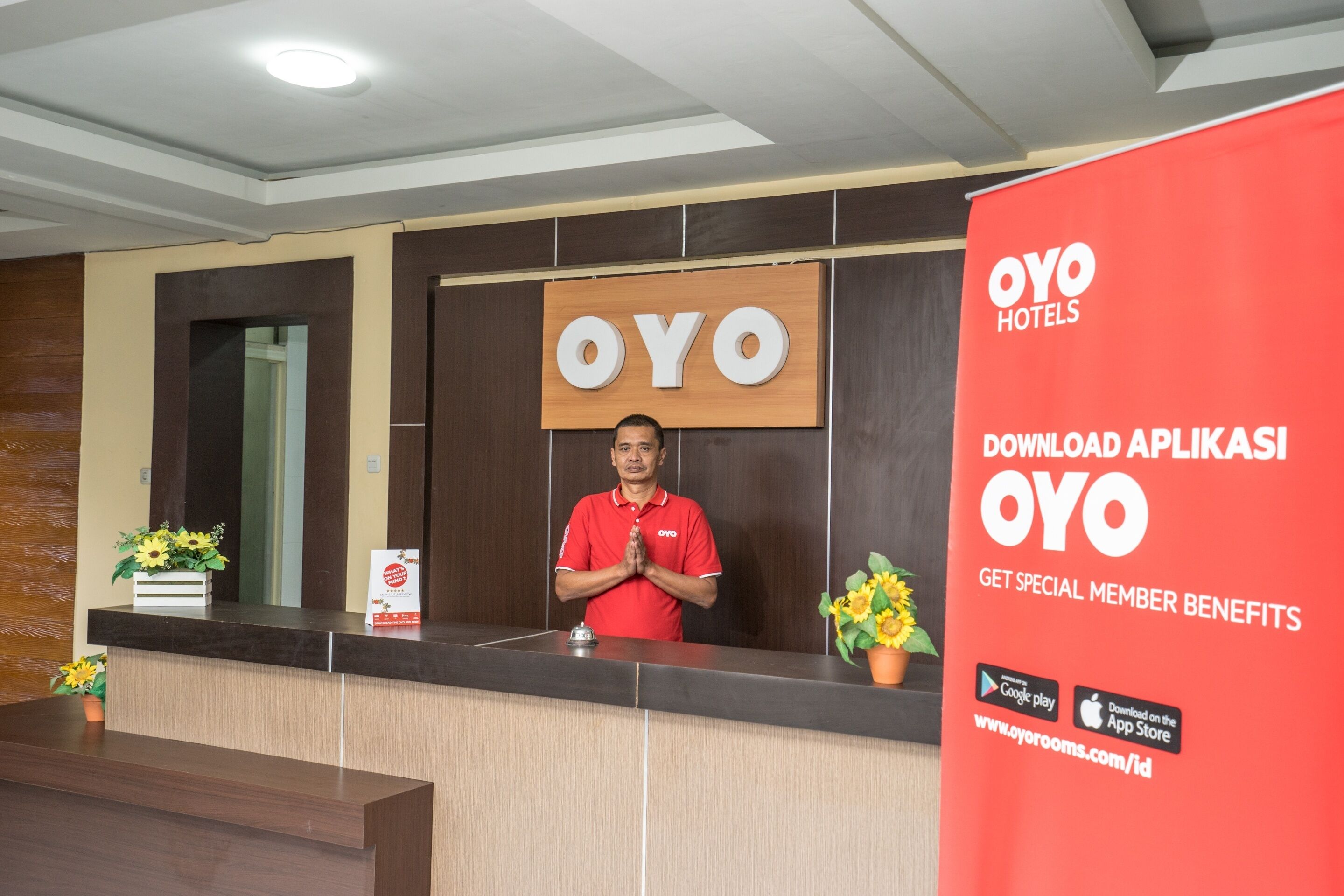 A reception desk with a wooden panel and a large OYO logo. There is a red promotional banner on the right.