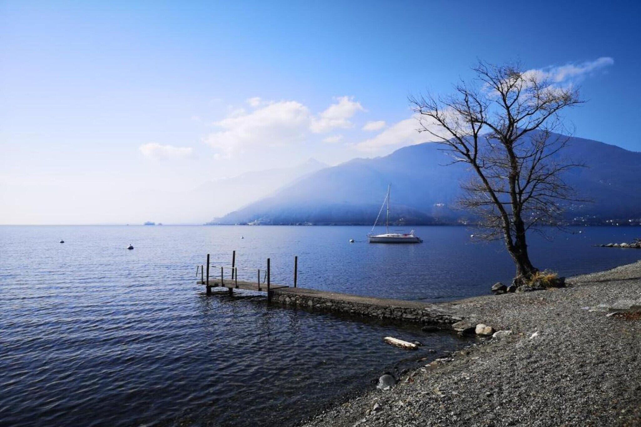 A calm lake with a dock, a sailboat, and a mountain in the background.