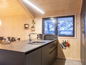 A modern kitchen with a granite countertop, stainless steel appliances, and a window with a view of snow-covered trees.