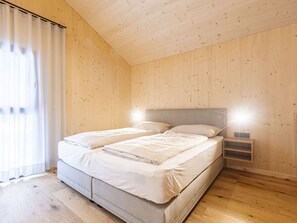Une chambre avec un plafond en bois, un lit avec une literie blanche et une table de chevet avec une lampe.
