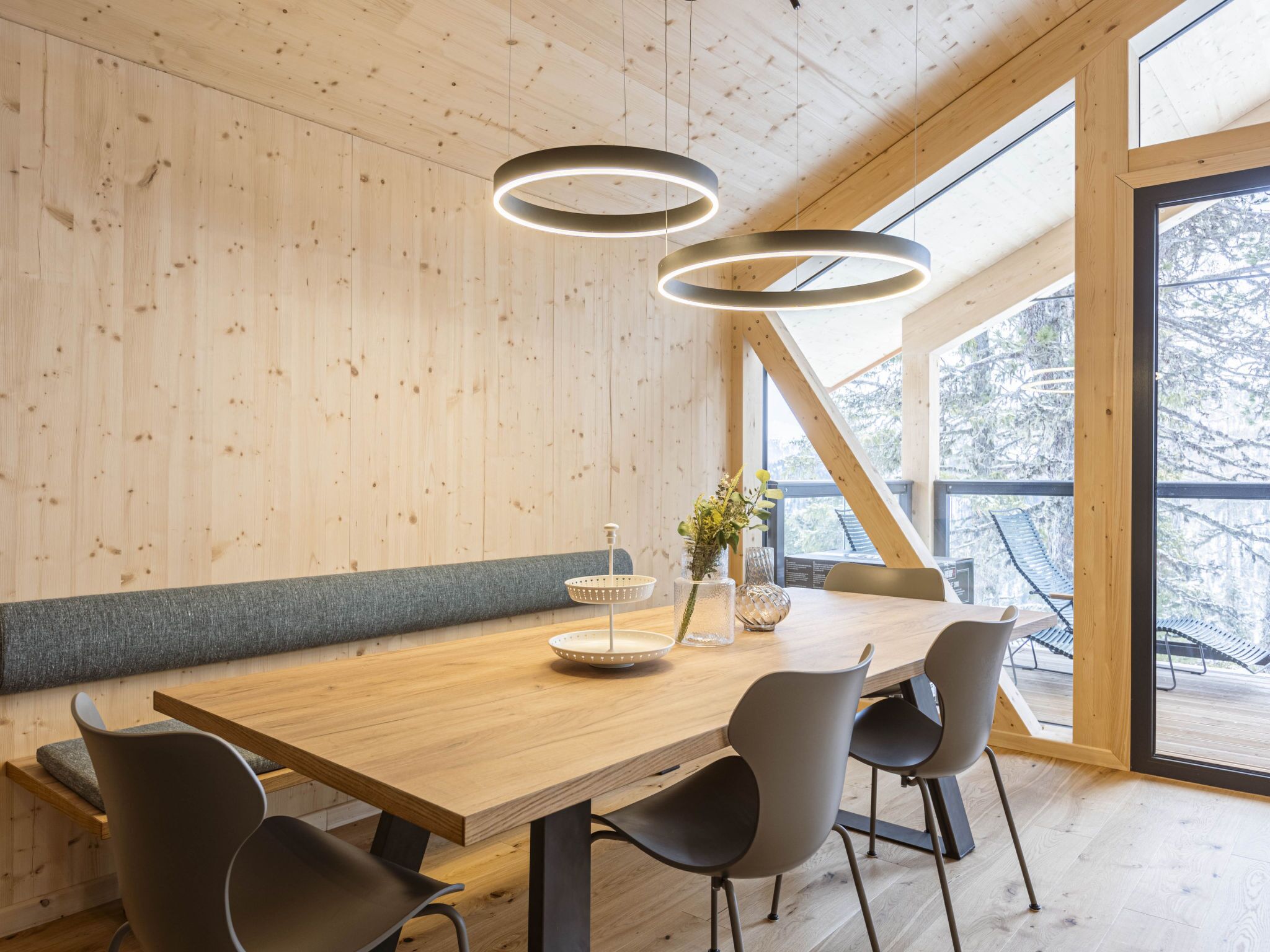 A modern dining area with a wooden table, black chairs, and a hanging light fixture.