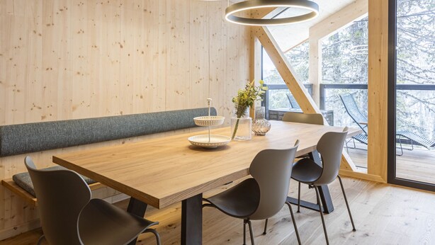 Un comedor moderno con una mesa de madera, sillas negras y una lámpara colgante.