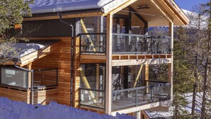 Una cabaña de madera con balcón, ventanas amplias y techo cubierto de nieve.