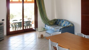Une pièce avec une table dont le plateau est en verre, un canapé aux motifs bleus et jaunes, une table à manger en bois et des chaises blanches.