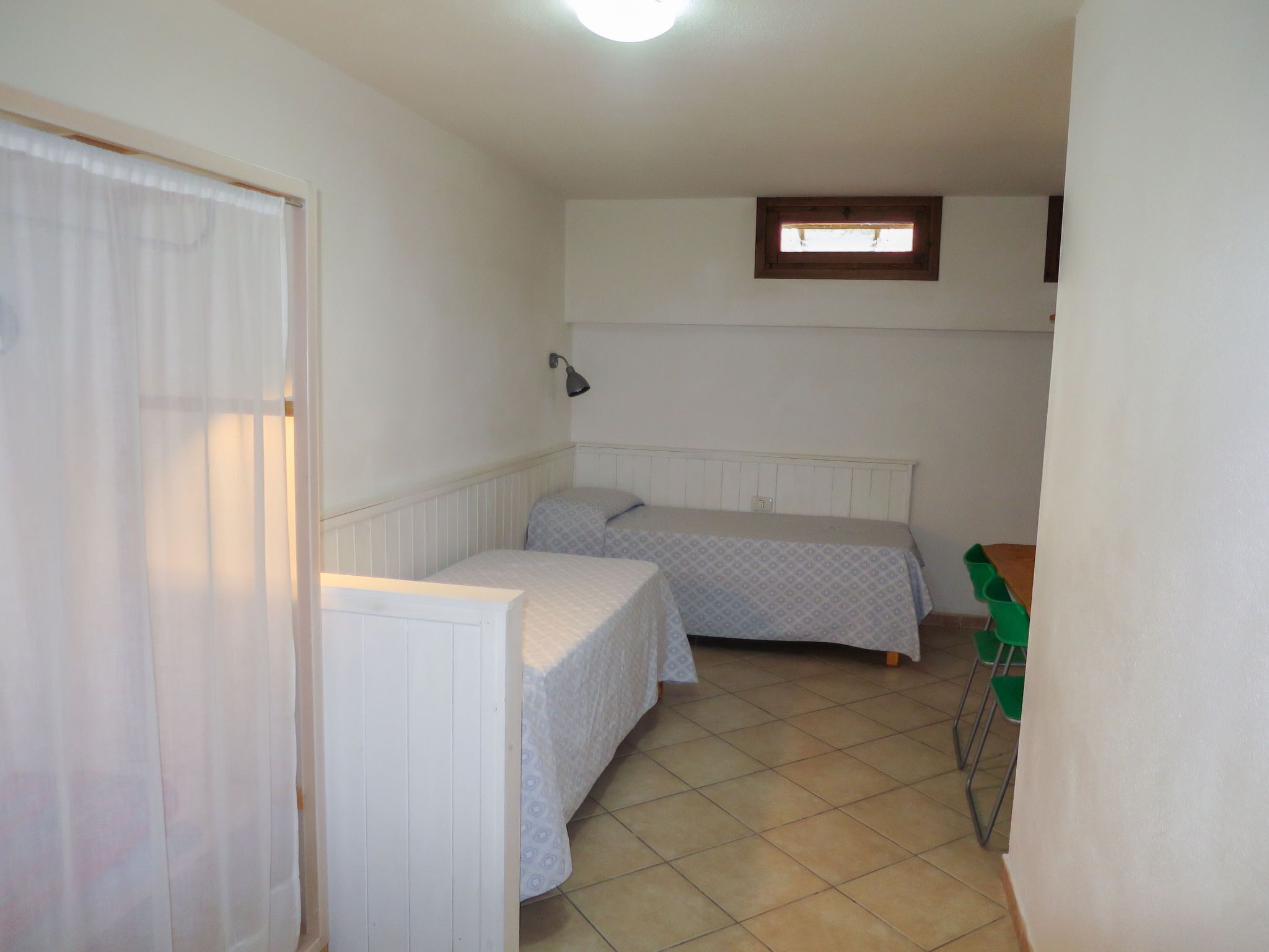 A small, clean room with two beds, a window, a lamp, and a door.
