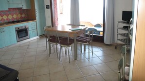 Una cocina moderna con gabinetes color turquesa, una zona de comedor con una mesa de madera y sillas metálicas, y un amplio ventanal con cortinas.