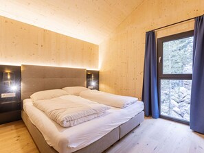 Ein Schlafzimmer mit Holzbalkendecke, einem Bett mit weißer Bettwäsche, zwei Nachttischlampen und einem Fenster mit Vorhängen.