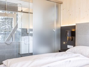 Une chambre à coucher moderne avec un lit, une table de chevet, une lampe fixée au mur et une cabine de douche en verre.