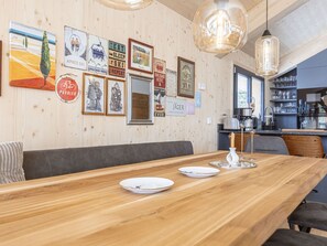 Une table à manger en bois, avec de l’assiette et des couverts, un coin bar avec des verres, et un mur décoré de panneaux anciens sur le thème du ski.