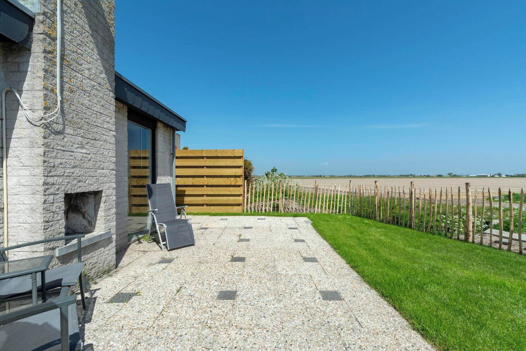 A stone building with a wooden door and a small window, a paved patio with a grill, and a grassy area with a fence.