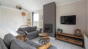 A modern living room with a grey sofa, a fireplace, a TV mounted on the wall, and a staircase leading to an upper floor.