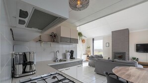A modern kitchen with a gas stove, coffee maker, and a built-in oven. There is a dining area with a table and chairs, and a living room with a sofa and a fireplace.