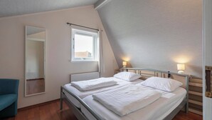 A bedroom with two beds, a mirror, a window, and a chair.