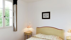 Une chambre à coucher avec un lit, une table de chevet avec une lampe, une fenêtre avec des rideaux et un tableau encadré au mur.