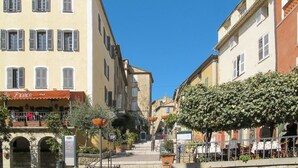Une rue bordée d’immeubles, avec un café et des tables en terrasse.