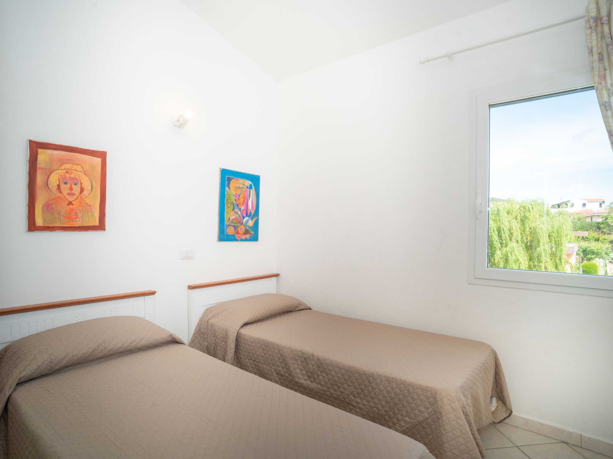 Une chambre avec deux lits, une fenêtre donnant sur un paysage verdoyant et deux tableaux accrochés au mur.