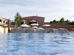 Zona de piscina con un edificio al fondo, con mobiliario exterior y sombrillas.