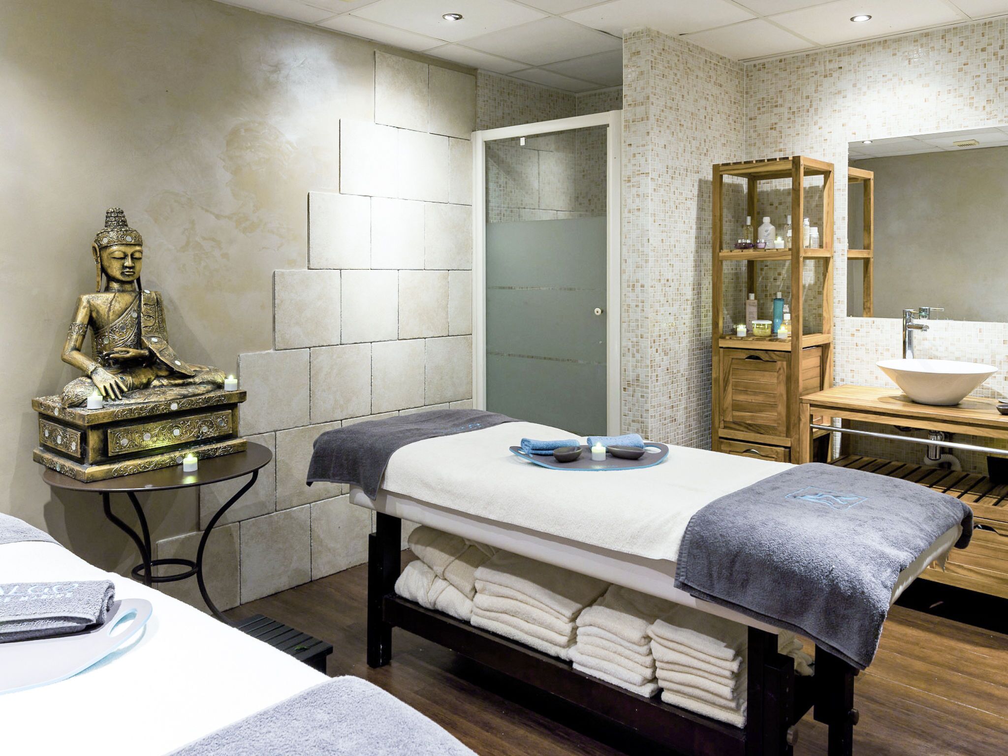 Un cuarto de spa con una estatua de meditación, una camilla de masaje y un mueble de madera con artículos de tocador.