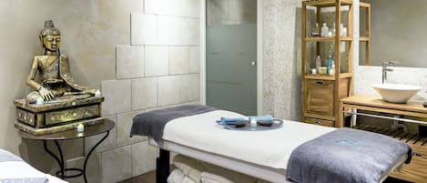 A spa room with a meditation statue, a massage table, and a wooden cabinet with toiletries.