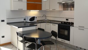 Una cocina moderna con armarios blancos, encimera negra, microondas, pileta, estufa y dos sillas.