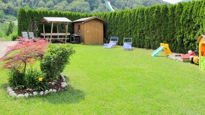 Un patio trasero con césped, una casita de juegos de madera, dos sillones de descanso y un tobogán.