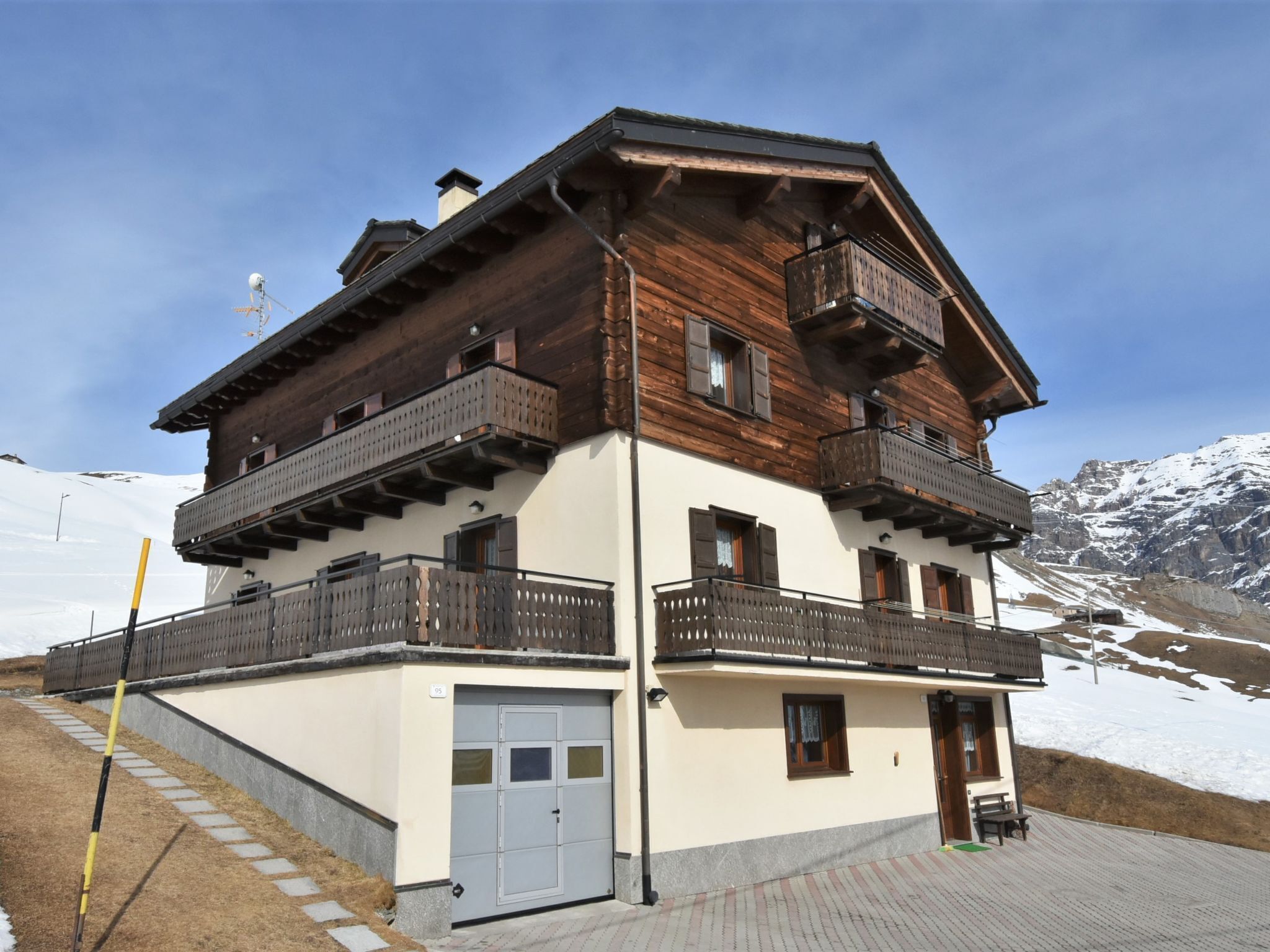 Una chaleta de varios pisos con balcones, un telesilla al fondo y un paisaje montañoso cubierto de nieve.