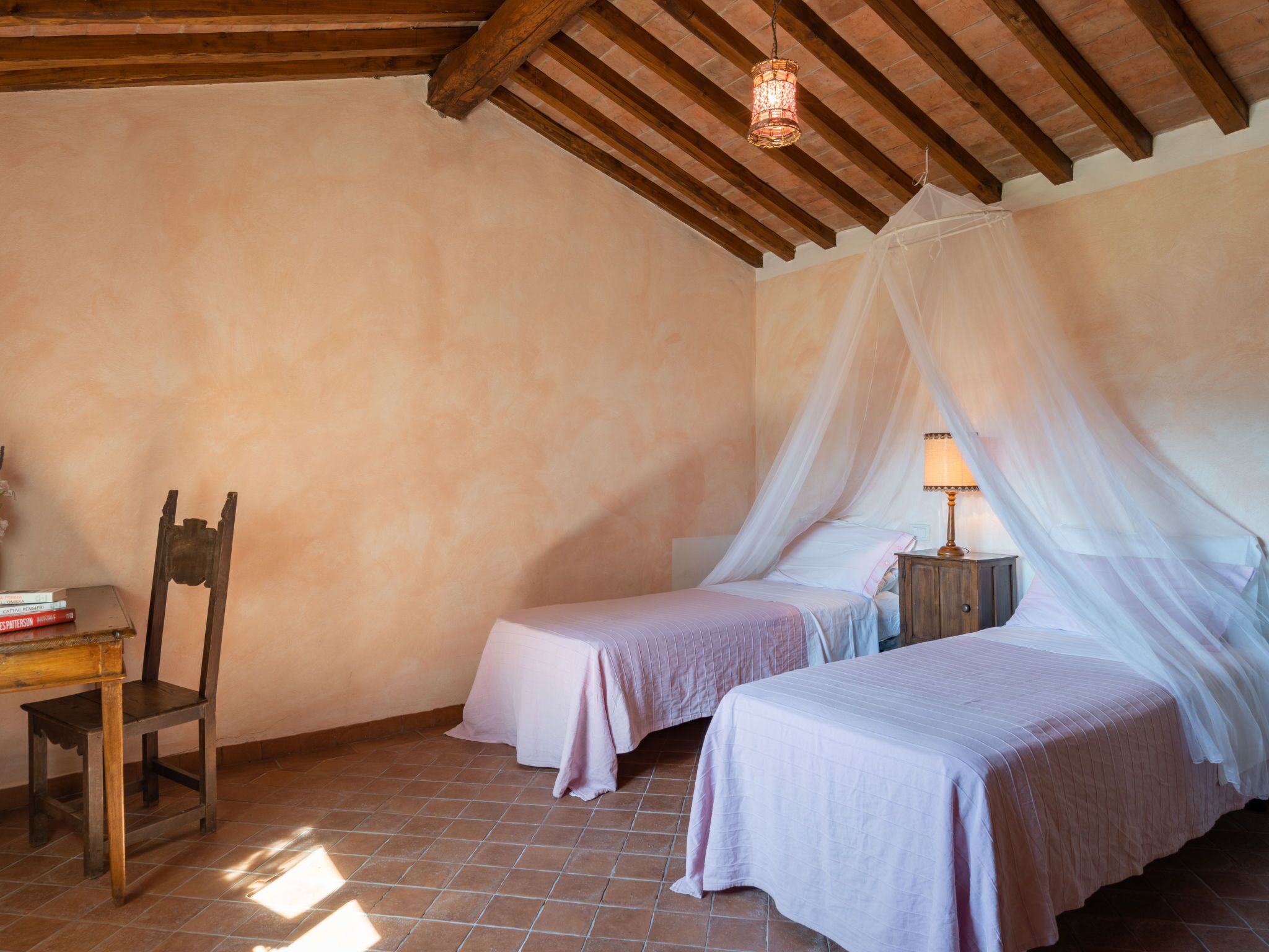 A bedroom with two beds, a chair, a nightstand, and a hanging light fixture.