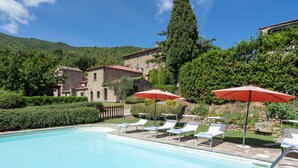 A pool area with lounge chairs and umbrellas, surrounded by stone buildings and greenery. - La Vittoria by Interhome (Cortona)