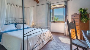 A four-poster bed with a canopy, a wooden dresser, a chair, and a window with a view of the landscape. - La Vittoria by Interhome (Cortona)