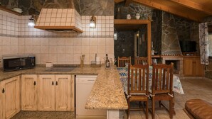 Een keuken met een stenen muur, houten kastjes, een granieten aanrechtblad en een eethoek met stoelen en een tafel.