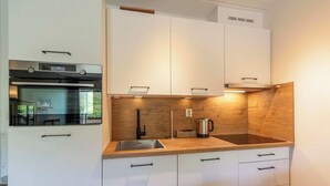A modern kitchen with white cabinetry, a built-in oven, a stainless steel sink, and a wooden countertop. - Apartment by Dutch Dunes with Sea Views (Callantsoog)