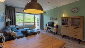 A modern living room with a sofa, TV, wooden cabinet, and a dining table. - Apartment by Dutch Dunes with Sea Views (Callantsoog)