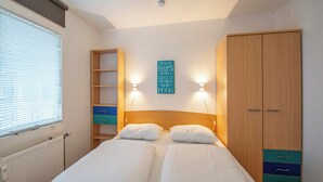 A bedroom with two beds, a wardrobe, a shelf unit, and a wall-mounted sign. - Apartment by Dutch Dunes with Sea Views (Callantsoog)