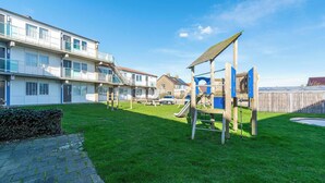 A residential area with a playground, a paved walkway, and a row of townhouses. - Apartment in Callantsoog near the dunes (Callantsoog)