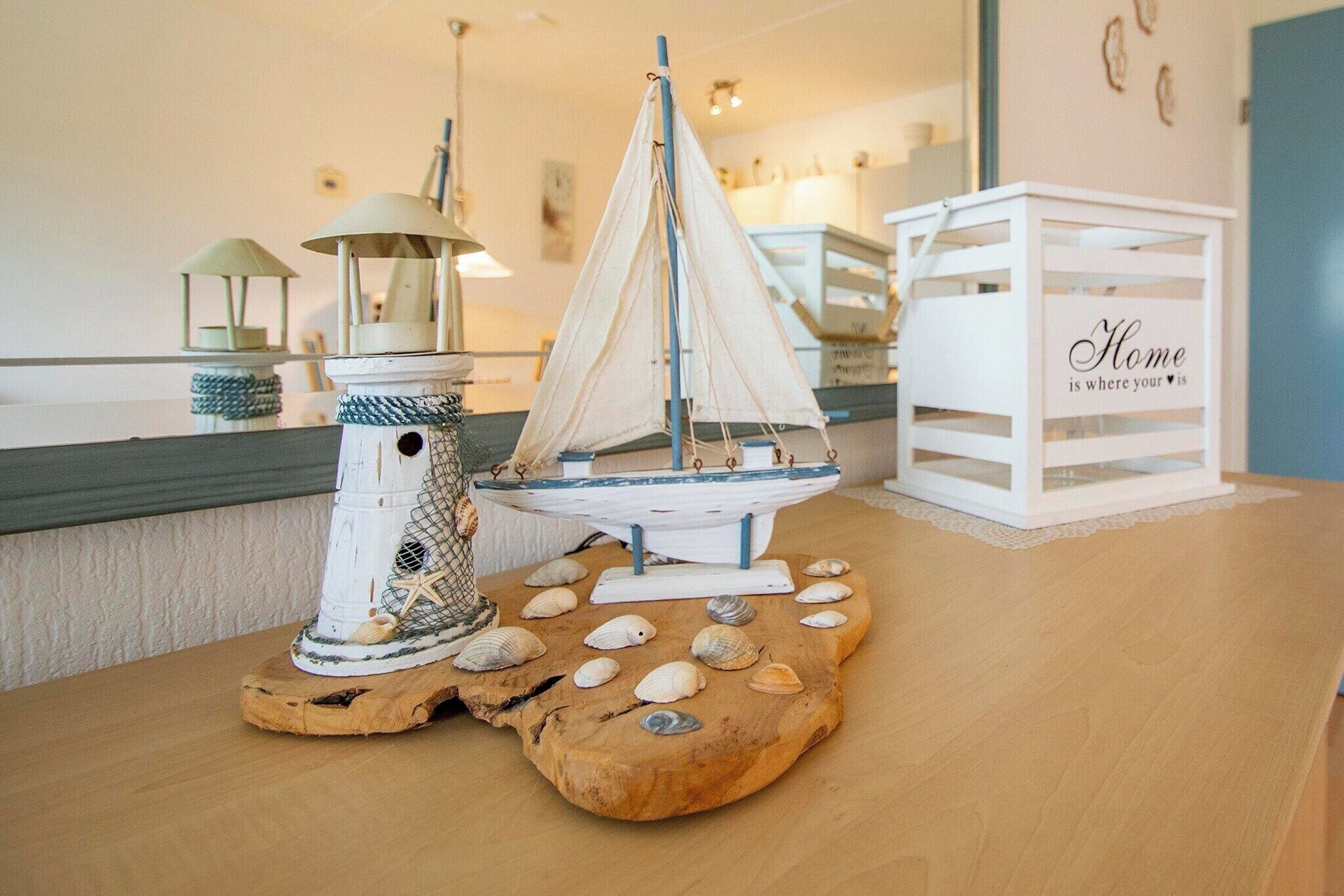 Ein Holztisch mit einem Modell eines Segelboots, einem Leuchtturm-Modell und einer weißen Kiste mit dem Aufdruck 'Home is where your heart is'.