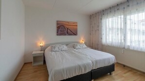 A bedroom with a bed, bedside tables, a painting, and a window with curtains. - Apartment in Callantsoog near the dunes (Callantsoog)