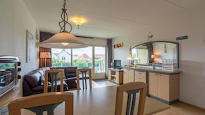 A modern living room with a sofa, chairs, a dining table, and a kitchen area with a TV and counter. - Apartment in Callantsoog near the dunes (Callantsoog)
