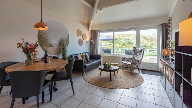 A modern living room with a dining area, a sofa set, a coffee table, and a large window with a view of greenery.