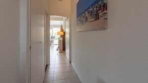 A hallway with a door leading to a room, a lamp, and a beach scene painting on the wall.