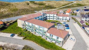 A coastal residential area with a multi-story building featuring balconies, a parking lot, and a view of the sea.