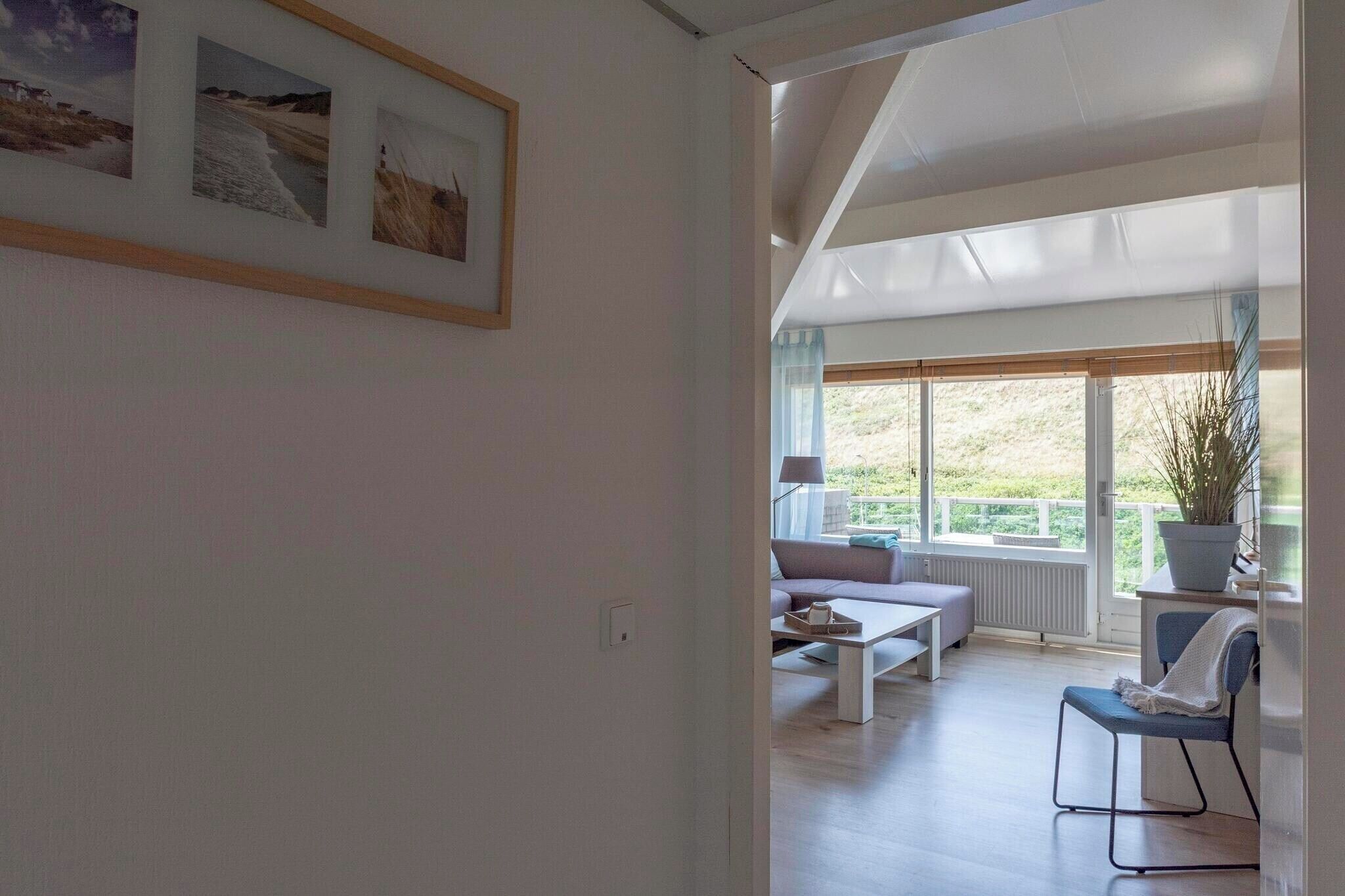 Una sala de estar moderna con un sofá, una mesa de centro y una silla. Hay un ventanal con vistas a la vegetación.