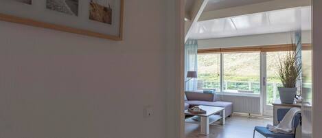 Una sala de estar moderna con un sofá, una mesa de centro y una silla. Hay un ventanal con vistas a la vegetación.