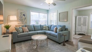 A living room with a sectional sofa, a round coffee table, a floor lamp, and artwork on the walls. - 6 Min Walk to Beach! Dog & Family Friendly, Ground Level Duplex Unit w/ Bunk Room & Covered Deck (Isle of Palms)