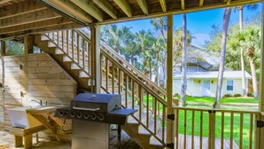 A covered outdoor area with a wooden deck, a grill, a sink, and a staircase leading to a house. - 6 Min Walk to Beach! Dog & Family Friendly, Ground Level Duplex Unit w/ Bunk Room & Covered Deck (Isle of Palms)
