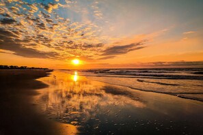 Une plage au coucher du soleil, avec un ciel dégagé et des vagues calmes.