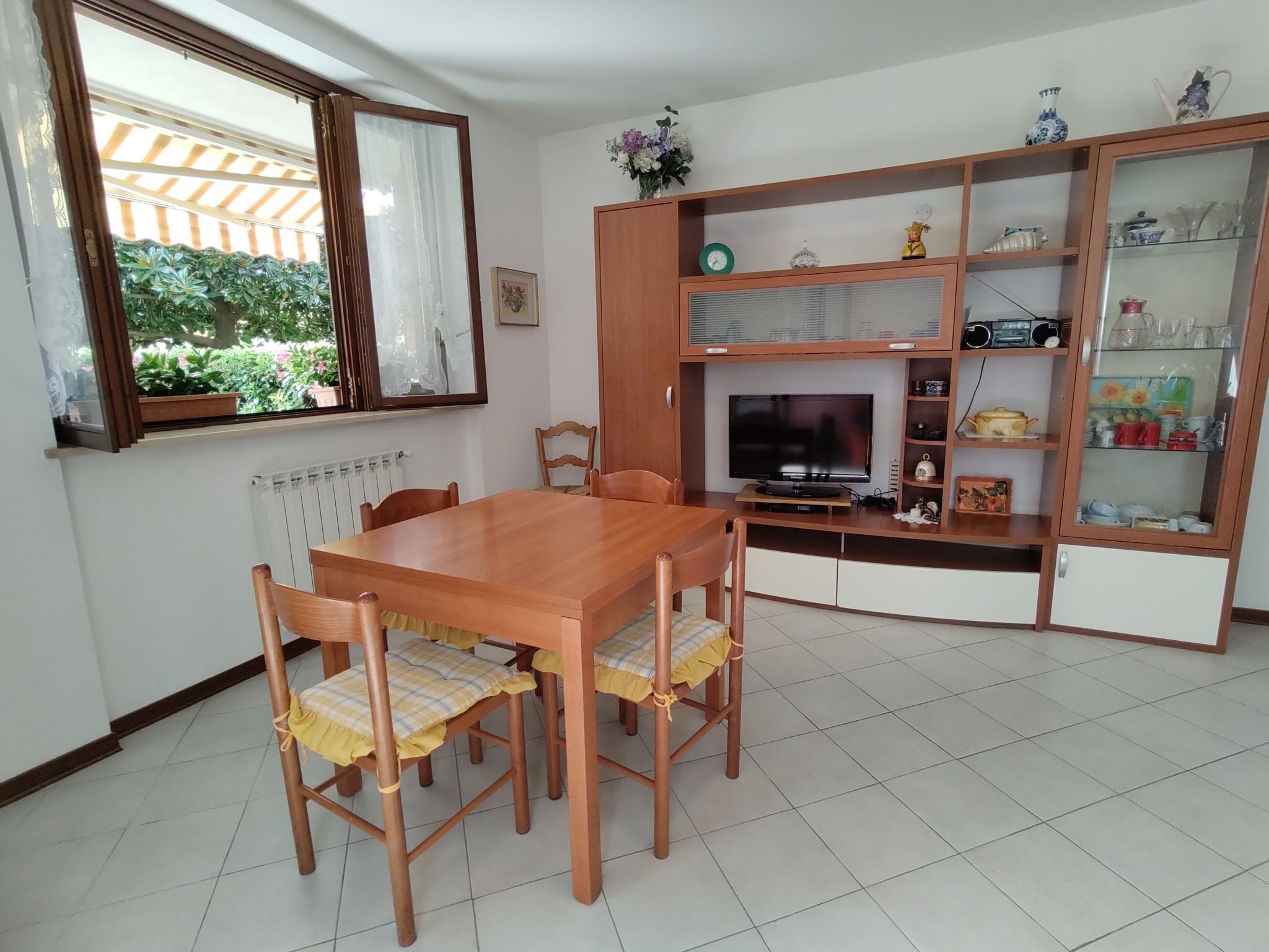 A dining area with a wooden table and chairs, a television, and a cabinet with glass doors.