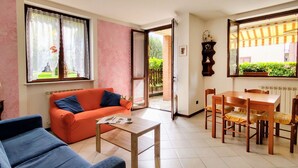 Ein Wohnzimmer mit einer Couch, einem Couchtisch, einem Esstisch mit Stühlen und einem großen Fenster mit Vorhängen.