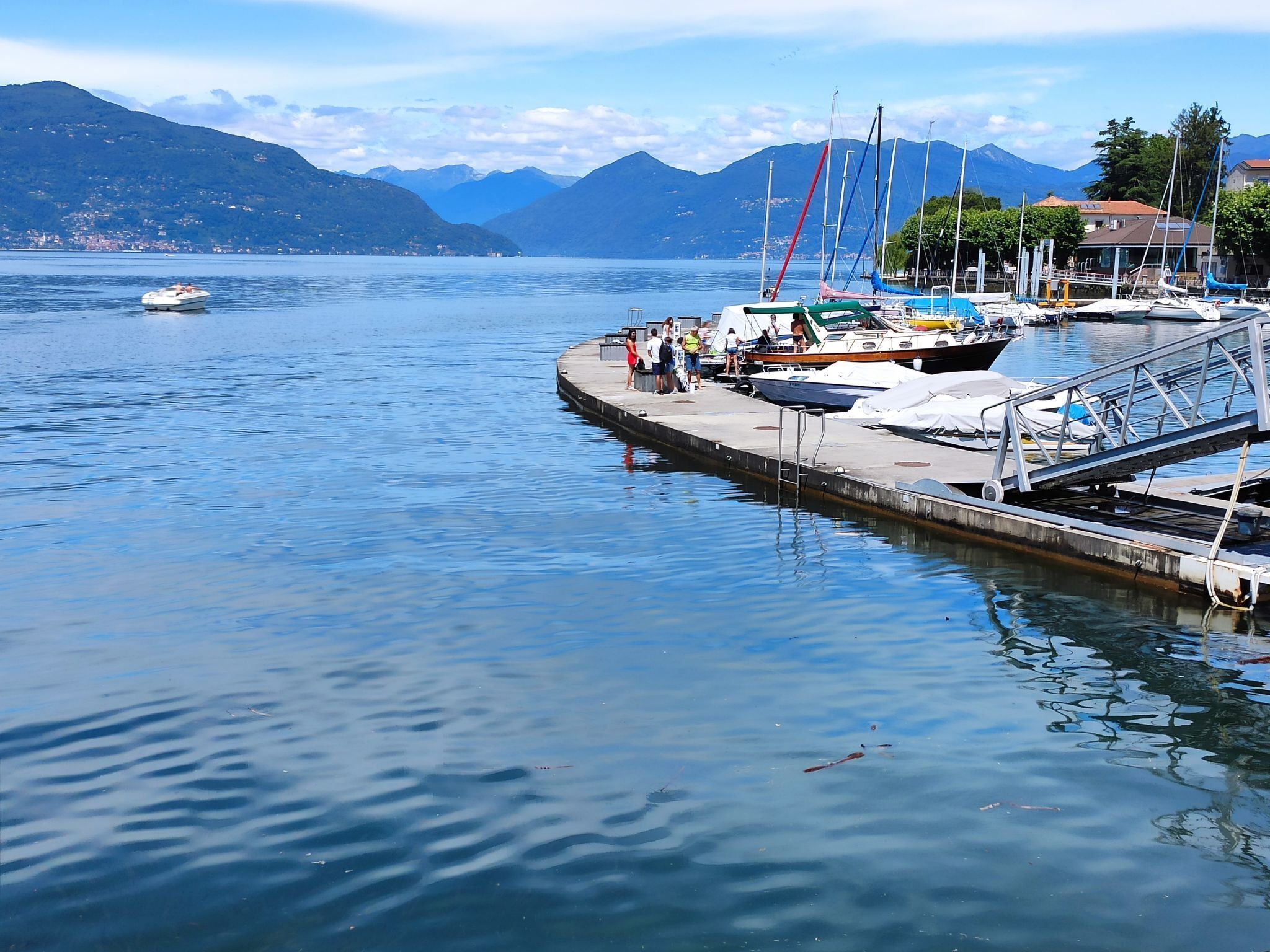 Un port de plaisance avec des bateaux amarrés, une petite embarcation sur l’eau et des montagnes en arrière-plan.