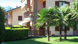 Ein zweistöckiges Haus mit Balkon, kleinem Garten und einer Palme.